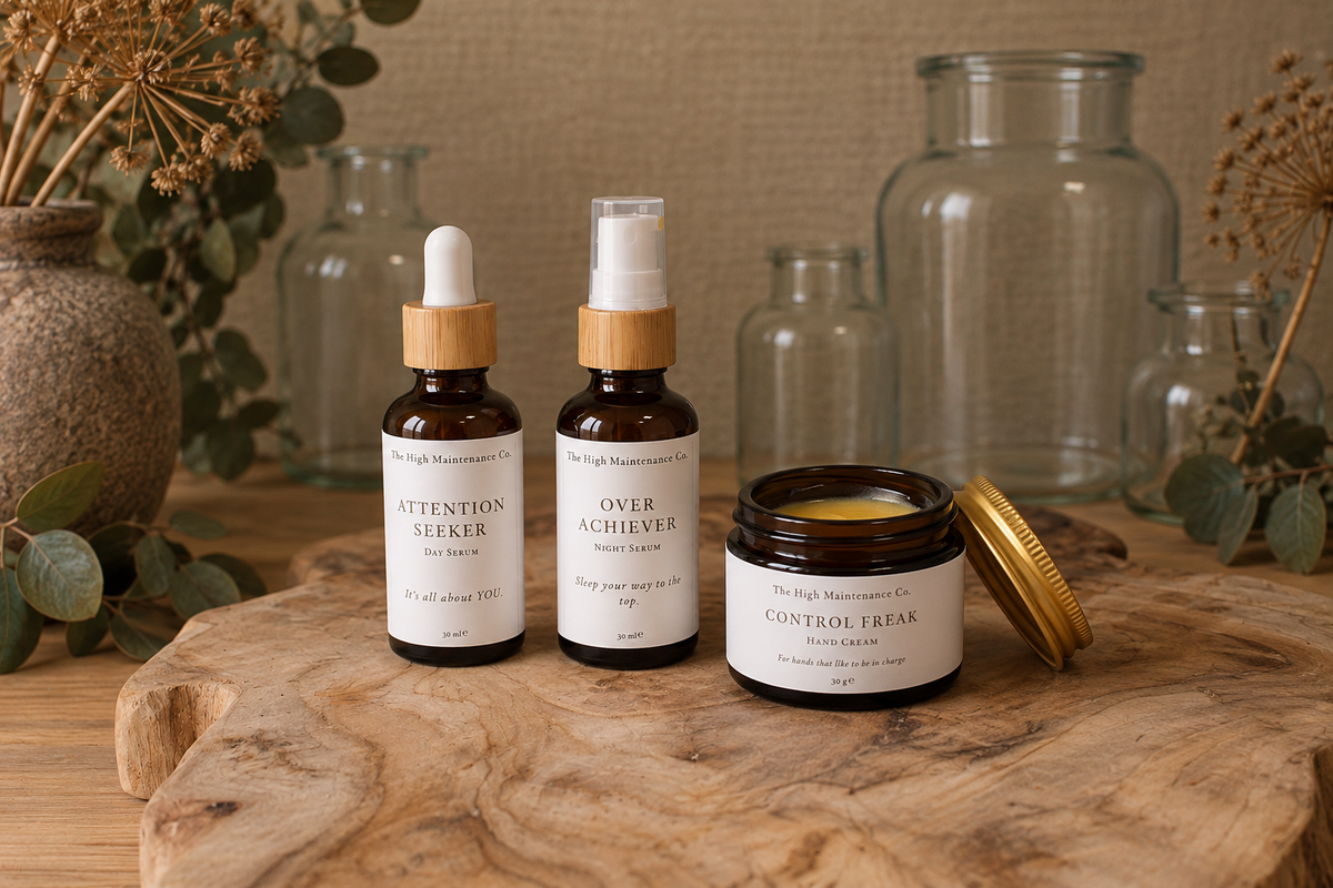 Three amber glass skin nourishing products from The High Measurement Co. are arranged on a rustic wood slab with dried botanicals and glass jars in the background.